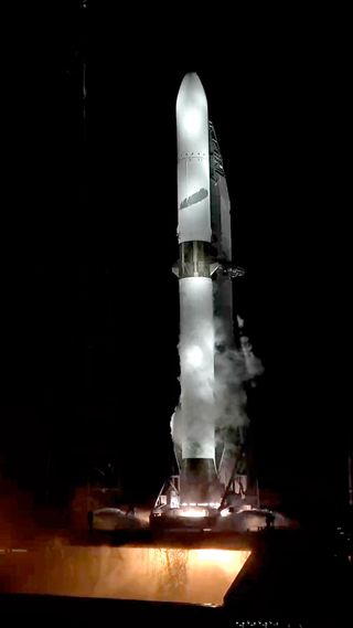 a tall white rocket test fires its engines on the launch pad