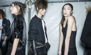 Three female models, one wearing a shiny black jacket with a black scarf with white polka dots, one in a blue plaid shirt and one in a black vest and black trousers