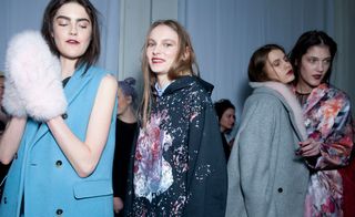 Four female models wearing looks from MSGM's collection. One model is wearing a blue sleeveless jacket and pink fluffy mittens. Next to her is a model wearing a light blue shirt and dark blue hoodie with multicoloured design at the front. The third model is wearing a grey coat and pink fluffy scarf. And the fourth model is wearing a multicoloured piece