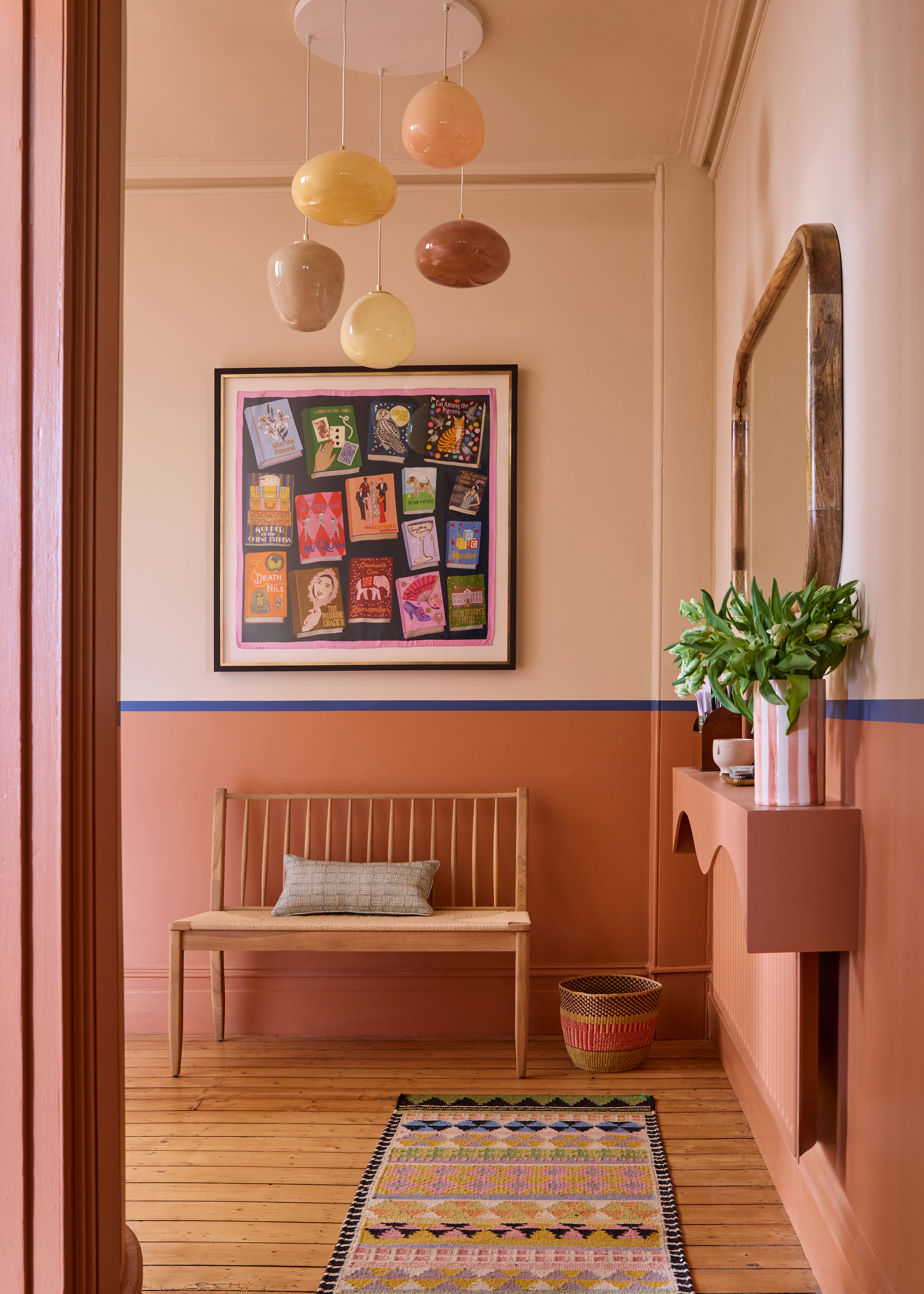 Image of a room painted in a light pink and terracotta pink color block with a royal blue stripe dividing the two paint colors. There is a bench seat, a woven basket, a colorful runner rug in the room
