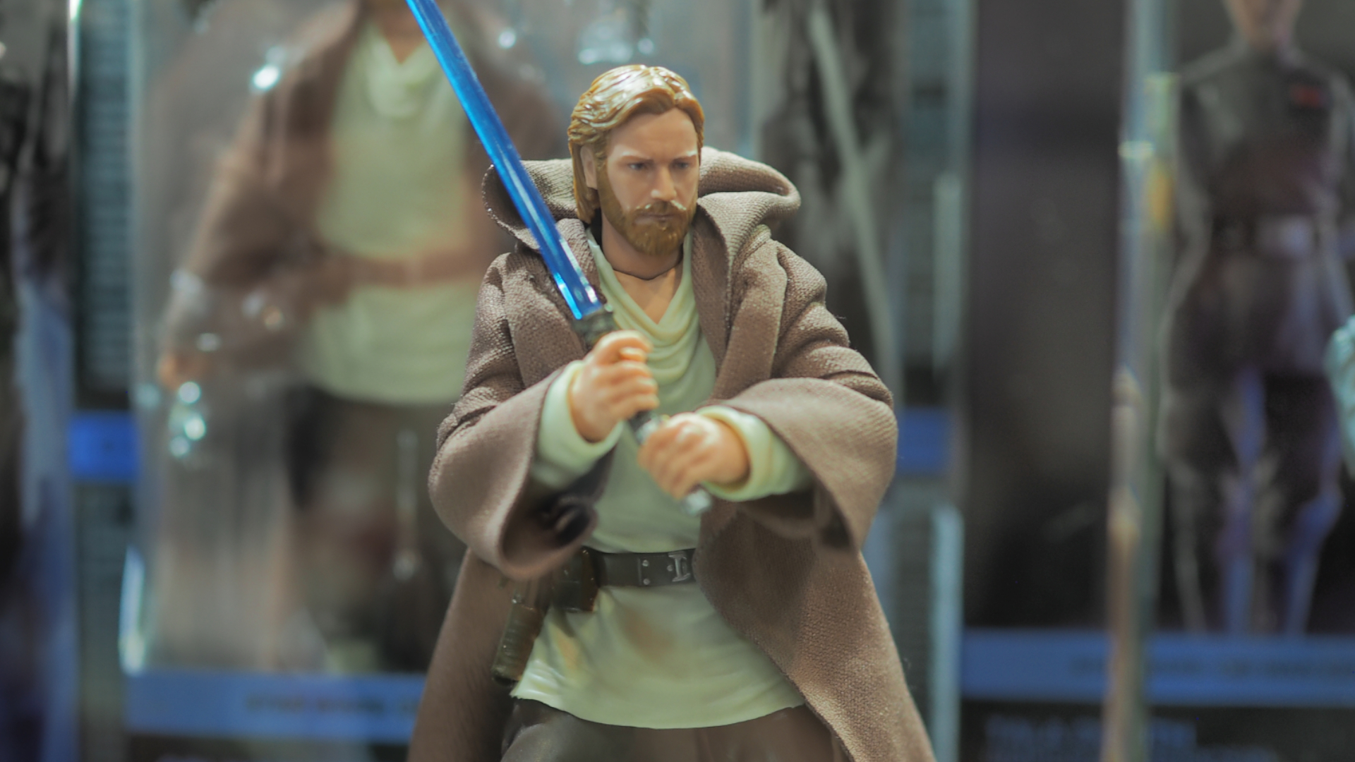 An Obi-Wan Kenobi action figure wielding a lightsaber, with boxes visible in the background