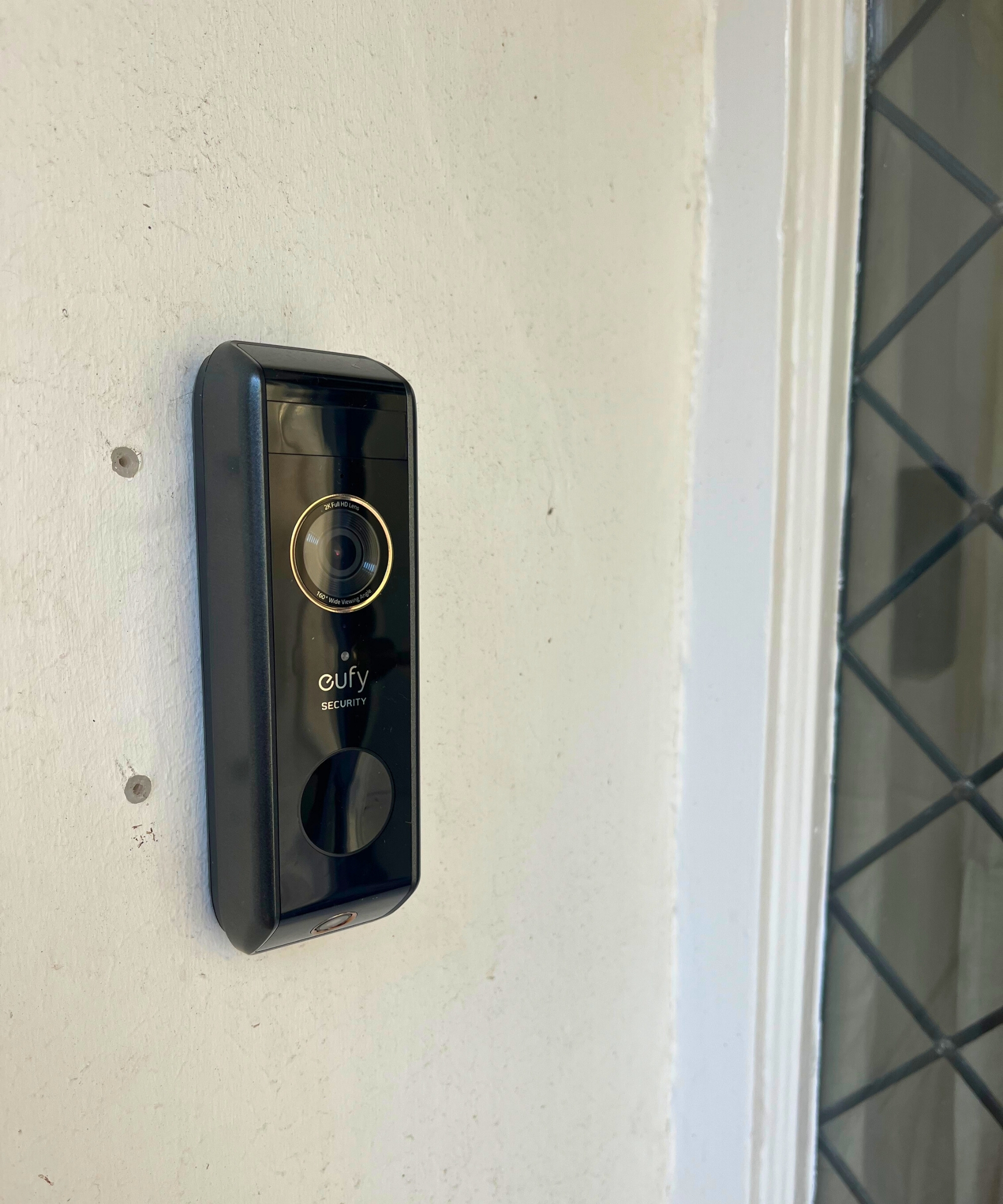 eufy S330 video doorbell mounted on white wall next to window.