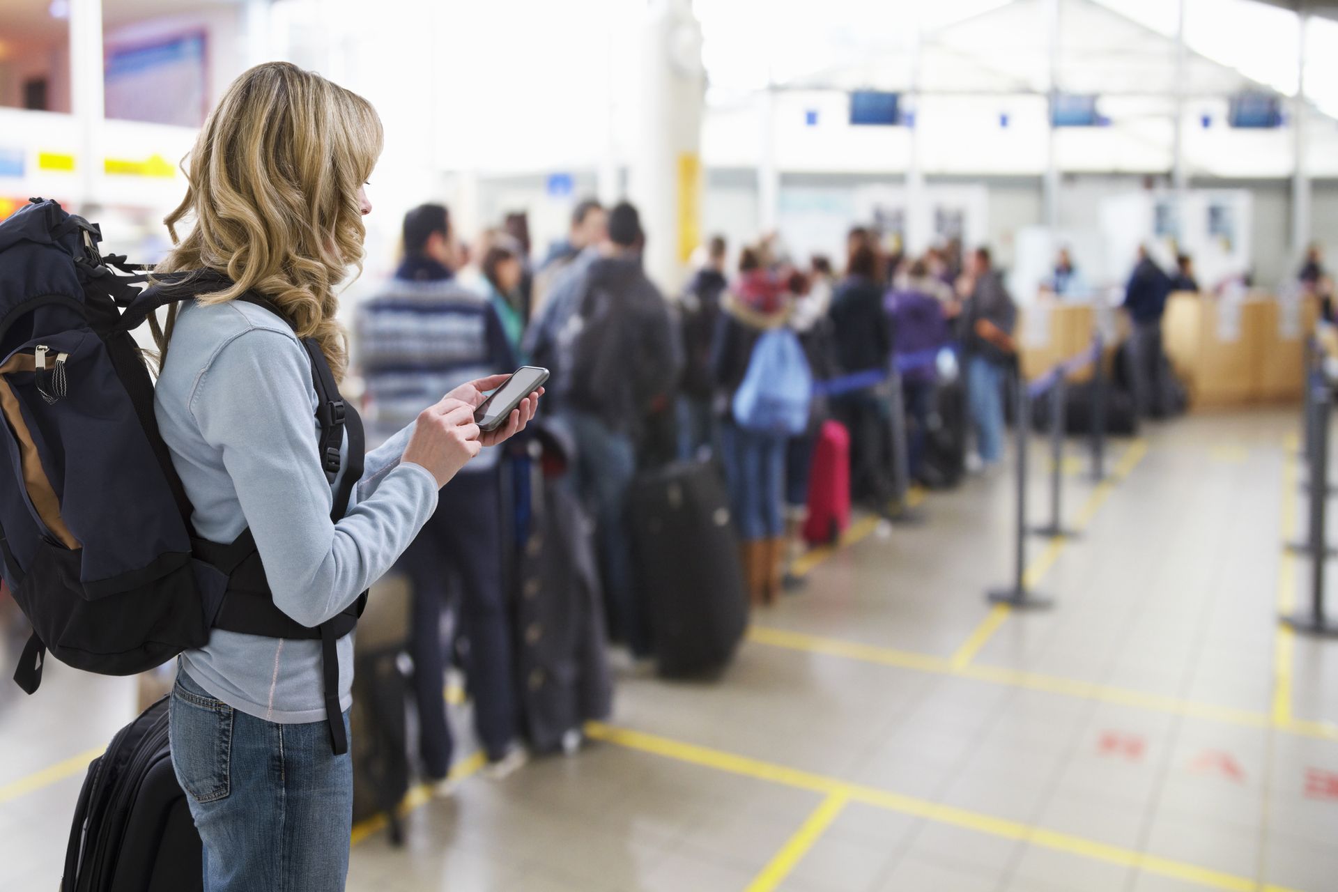 Female traveller texting at airport check-in desk.