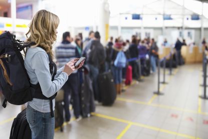 Female traveller texting at airport check-in desk.