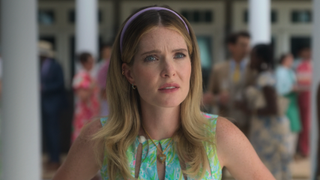 Meghann Fahy looking concerned in green floral dress, purple headband and basket necklace in Sirens TV show