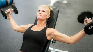 Woman performs incline chest flye with dumbbells in a gym