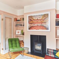 Black log burner in a light pink living room with artwork on the chimney and a statement green chair