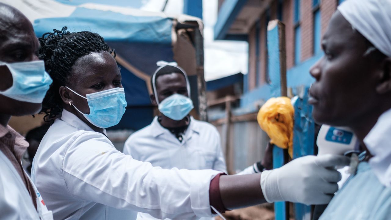 Healthcare workers in Kenya check a patients temperature while dressed in PPE.