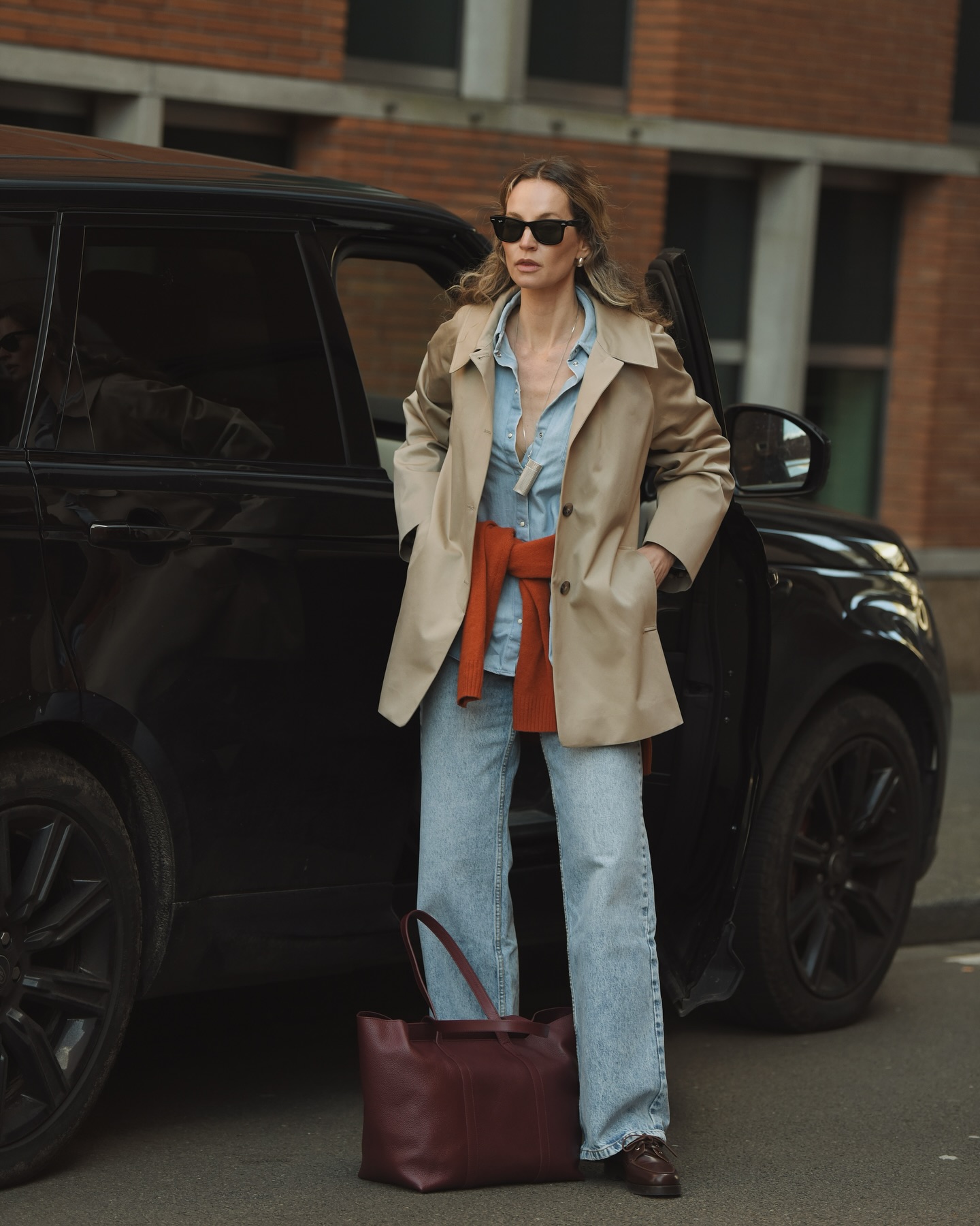 Woman wearing a short trench coat with light wash jeans.