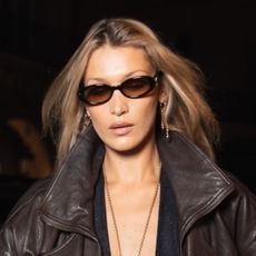 Bella Hadid wearing a brown leather jacket, black capri pants, and pendant necklace