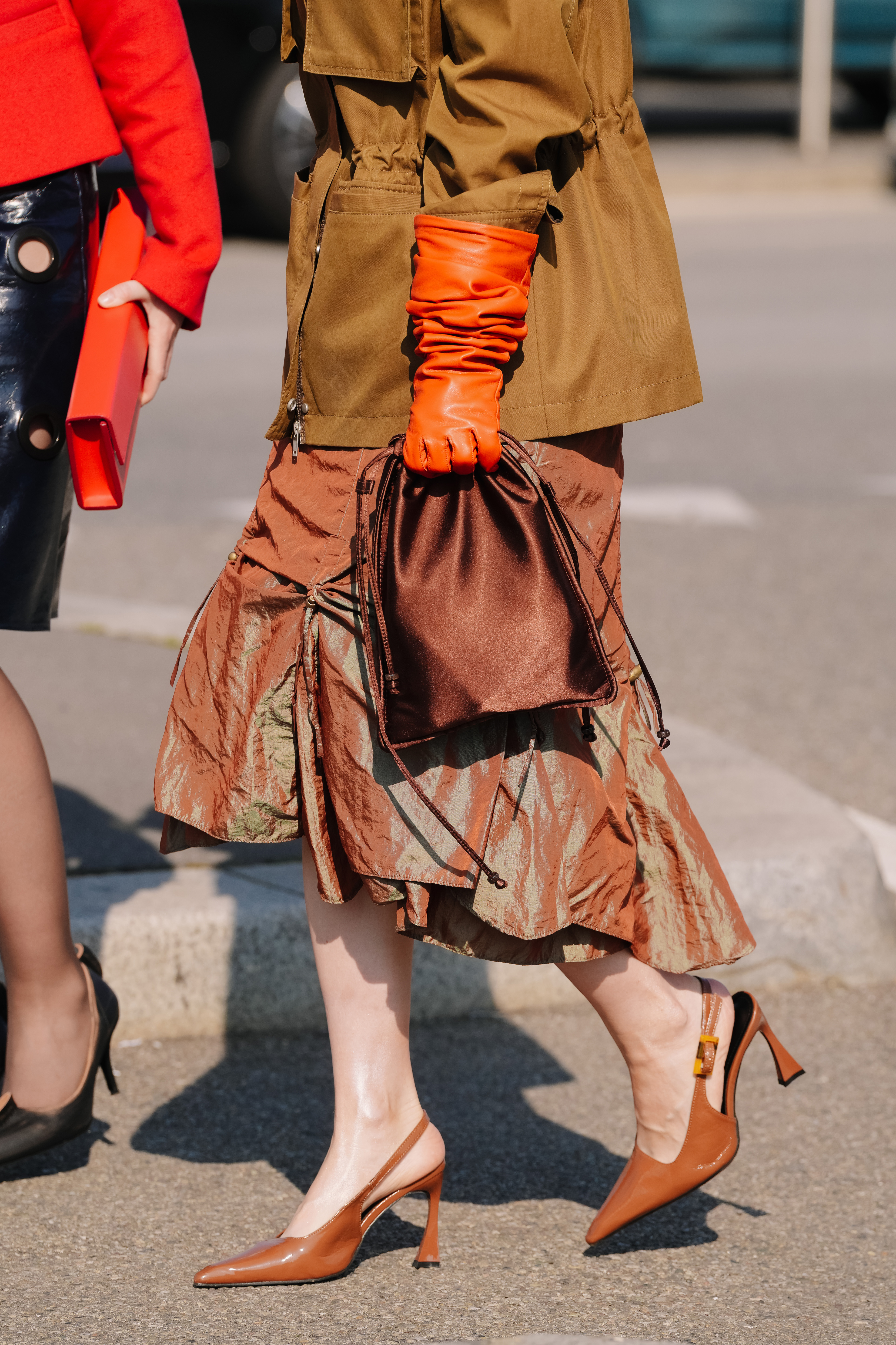 MILAN, ITALY - FEBRUARY 26: A guest is seen wearing a tan brown utility jacket, orange gloves, a midi skirt, pointed heels, a Prada bag during the Milan Fashion Week - Womenswear Fall/Winter 2026/2027 on February 26, 2026 in Milan, Italy. (Photo by Alena Zakirova/Getty Images)