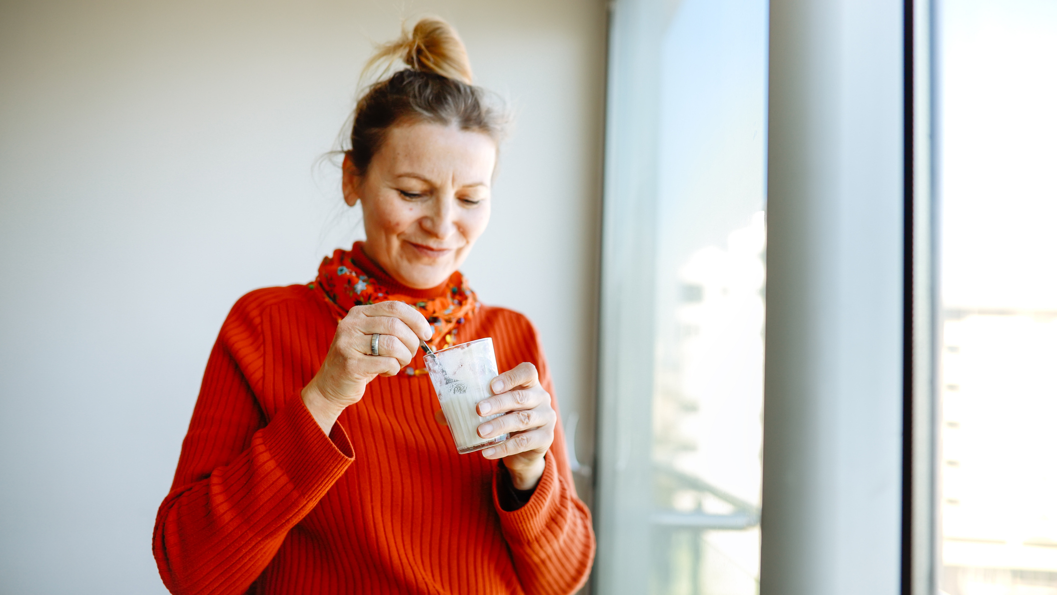 Woman eating yoghurt with a spoon from a glass