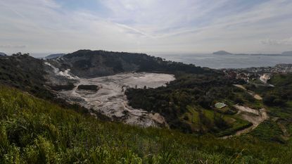 An aerial view of a caldera surrounded by lush countryside with the ocean in the background