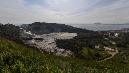 An aerial view of a caldera surrounded by lush countryside with the ocean in the background