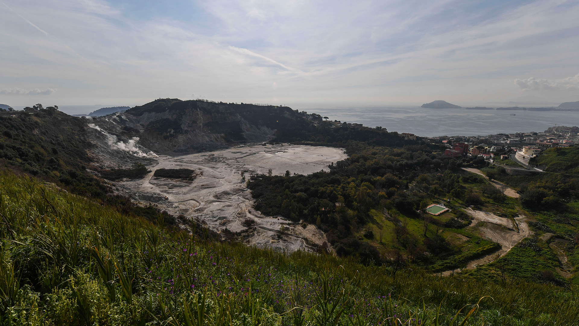An aerial view of a caldera surrounded by lush countryside with the ocean in the background