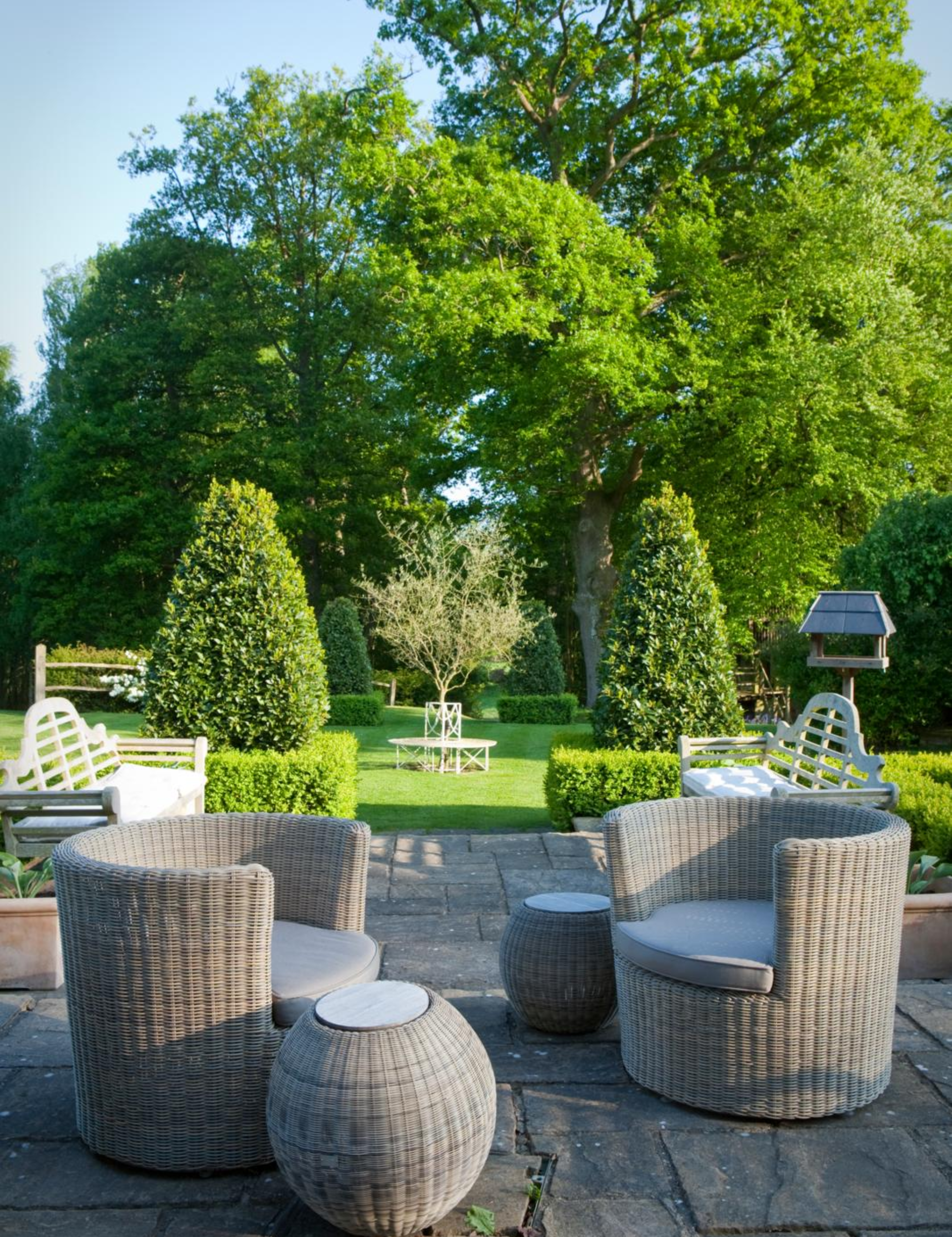 Grassy outdoor patio area featuring a pair of woven wicker club chairs accented by matching ottomans.