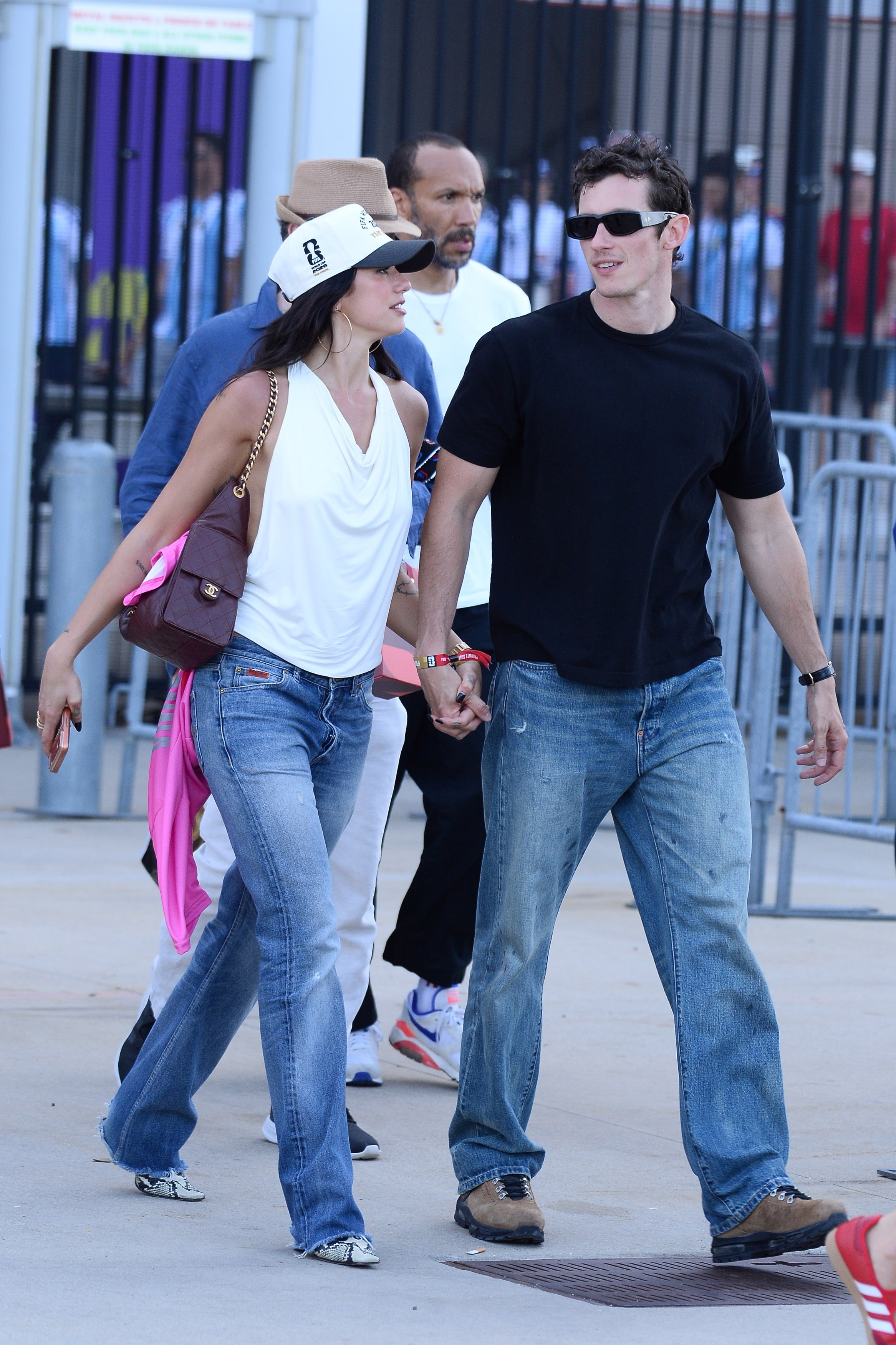 Dua Lipa and Calum Turner exit the World Cup holding hands. Dua wears straight-leg jeans with snakeskin shoes and a white halterneck top.