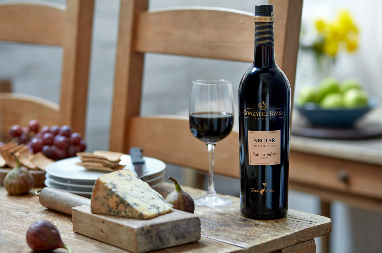 A bottle of sherry on a wooden table with cheese