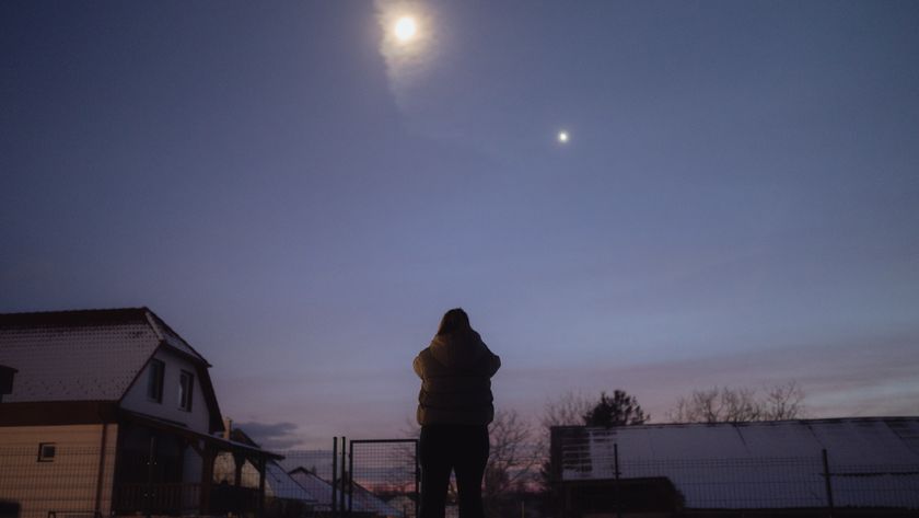 a woman stands looking up at the bright moon and saturn in the sky.