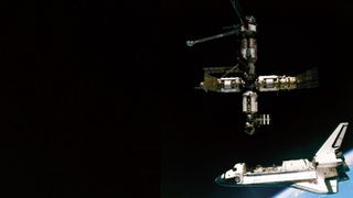 a space shuttle with open cargo bay hangs separated from a space station floating above.