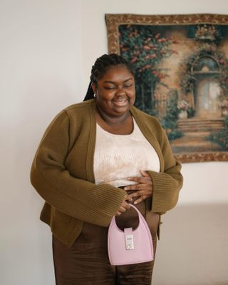 Woman in olive green cardigan, white top, and brown pants.