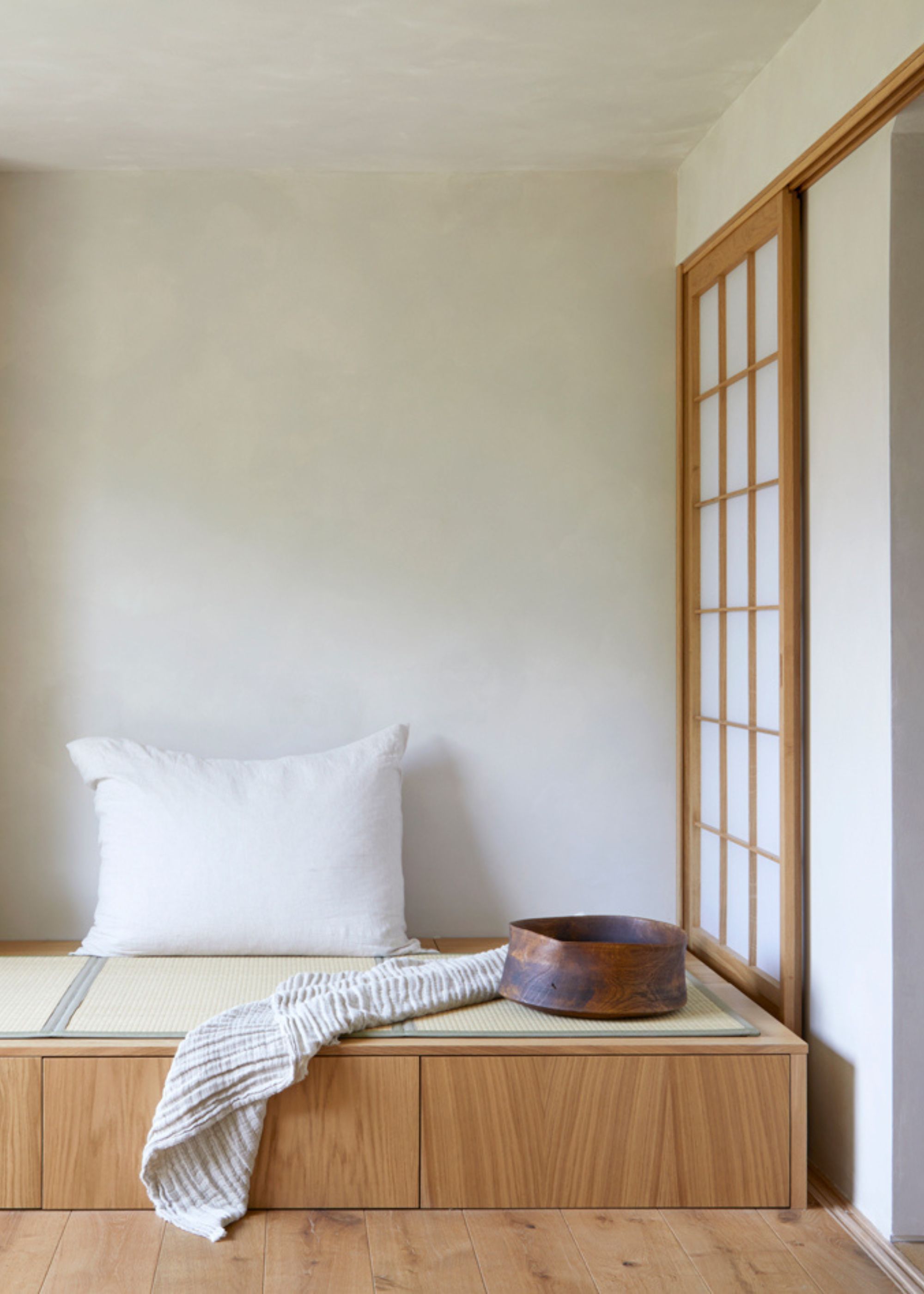 A Japanese raised wood bed with a tatami mat, a textured throw, a shoji screen, and a pillow