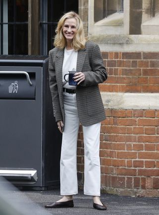 Julia Roberts wears an oversized blazer, light-wash jeans, and black ballet flats while carrying a cup of coffee on a city street.