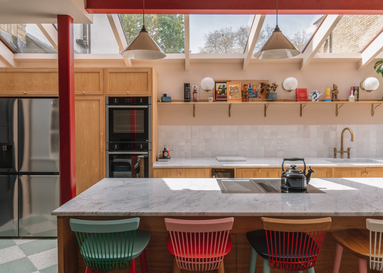 a kitchen with kitchen island seating with different colored bar stools and overhead lighting and skylights