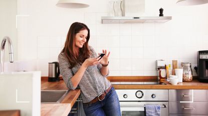 Woman looking at her phone in the kitchen, googling menopause symptoms