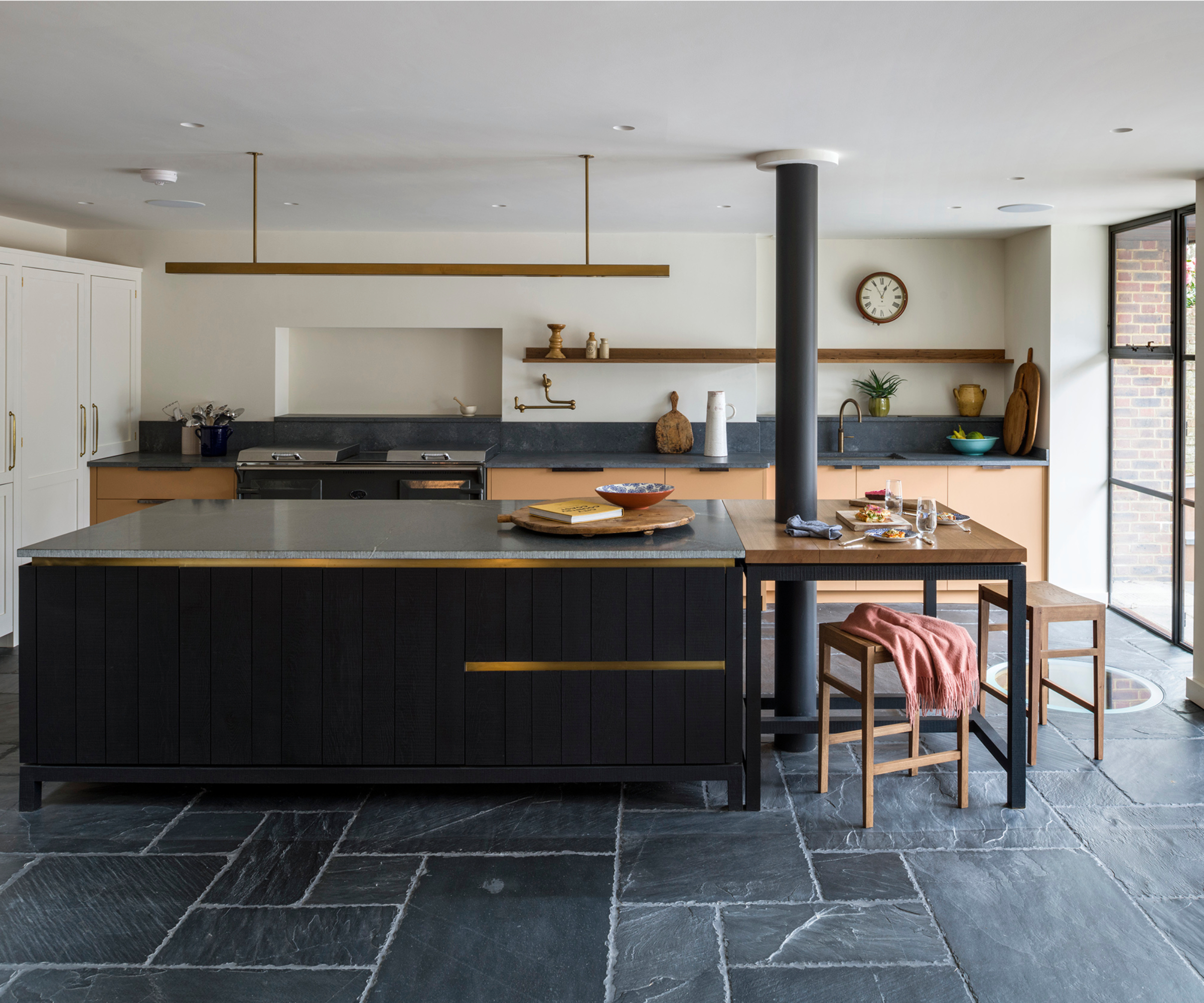 kitchen with slate floor and island with dark black cabinets, brass trim on door and long brushed brass slim light above island