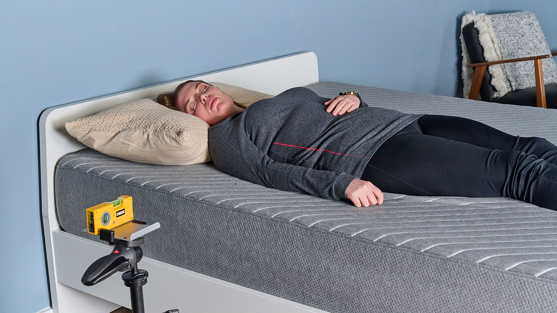 This image shows our sleep tester Ruth Jones lying on the Siena Memory Foam Mattress during the pressure relief test. She is lying on her back on the left hand side of the mattress, with a pillow for support. A laser, balanced on a tripod in the front of the shot, projects a red line on to her body. The line is positioned to follow the line of her spine. As the laser and her body are both aligned, we can see this is a good mattress for back sleepers.
