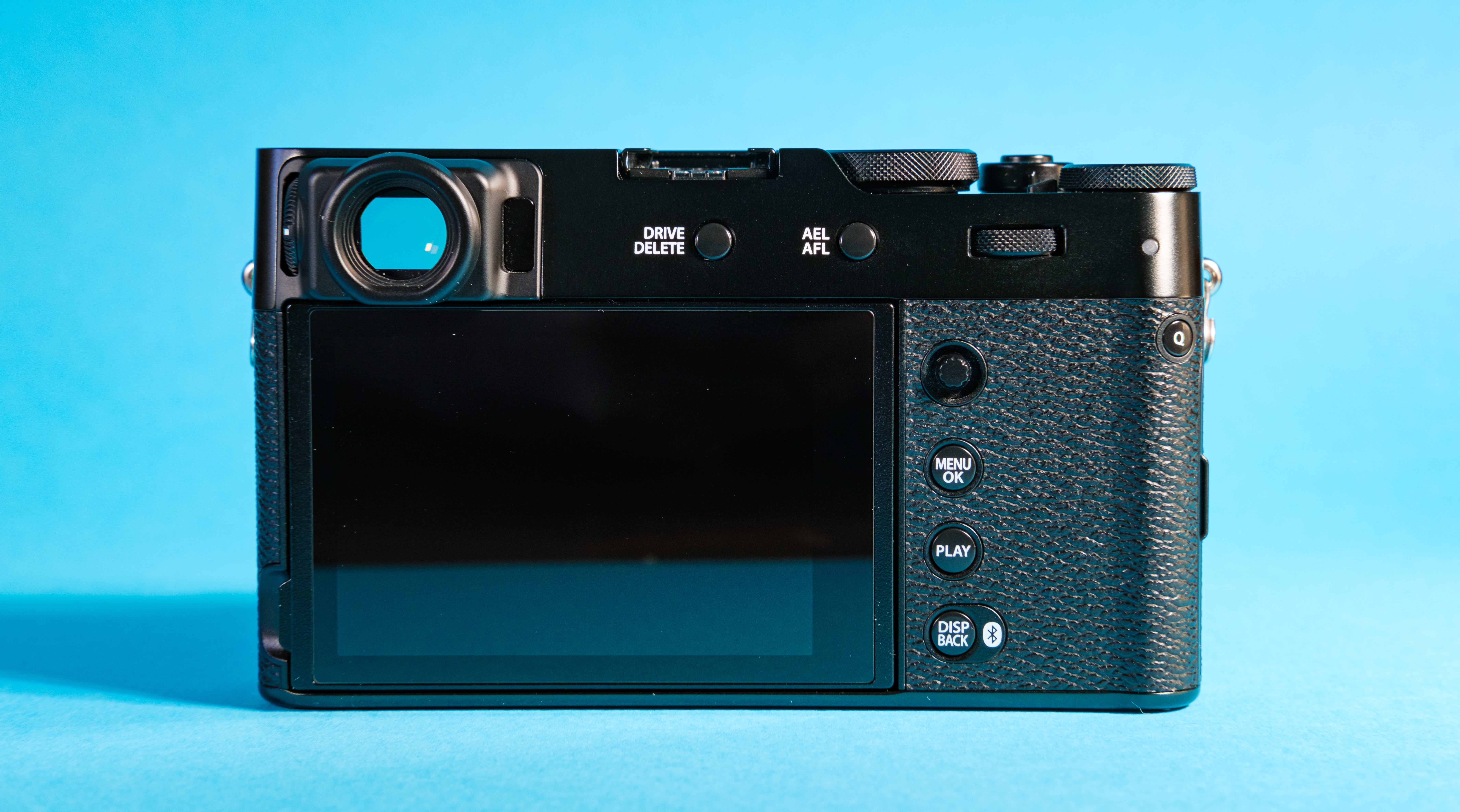 The Fujifilm X100VI mirrorless camera against a blue background  with the rear screen showing.