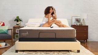 A woman sits with her feet together in the middle of a Cocoon by Sealy Chill Mattress