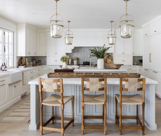 white kitchen with light gray island, gold pendants and wooden and rattan bar stools