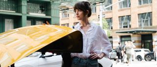 Dakota Johnson in Materialists looking to her right and placing her hand on the trunk of a yellow car.