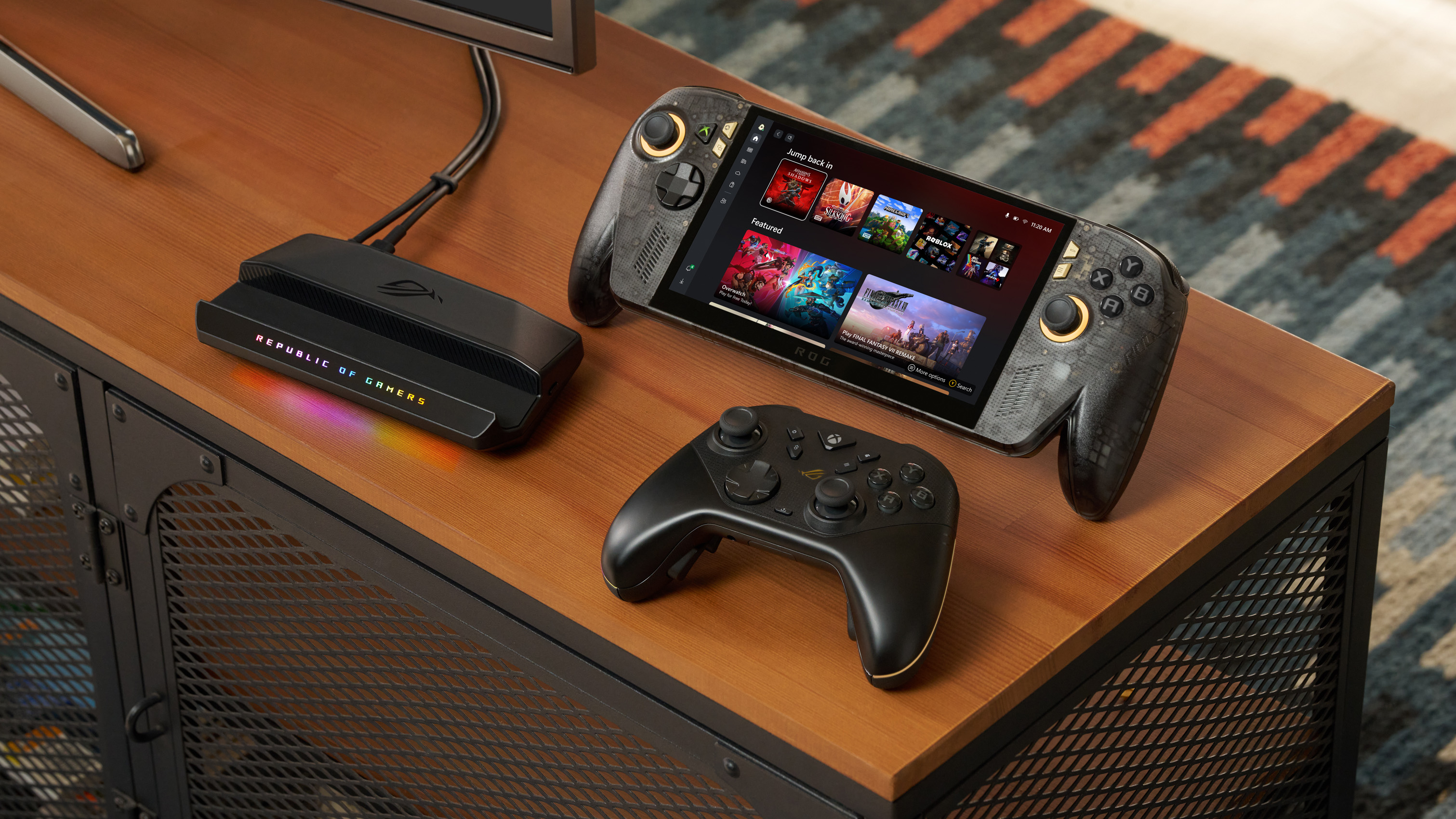 ROG Xbox Ally X20 handheld sitting upright on a desk setup alongside a black wireless controller and an RGB-lit Republic of Gamers dock station.