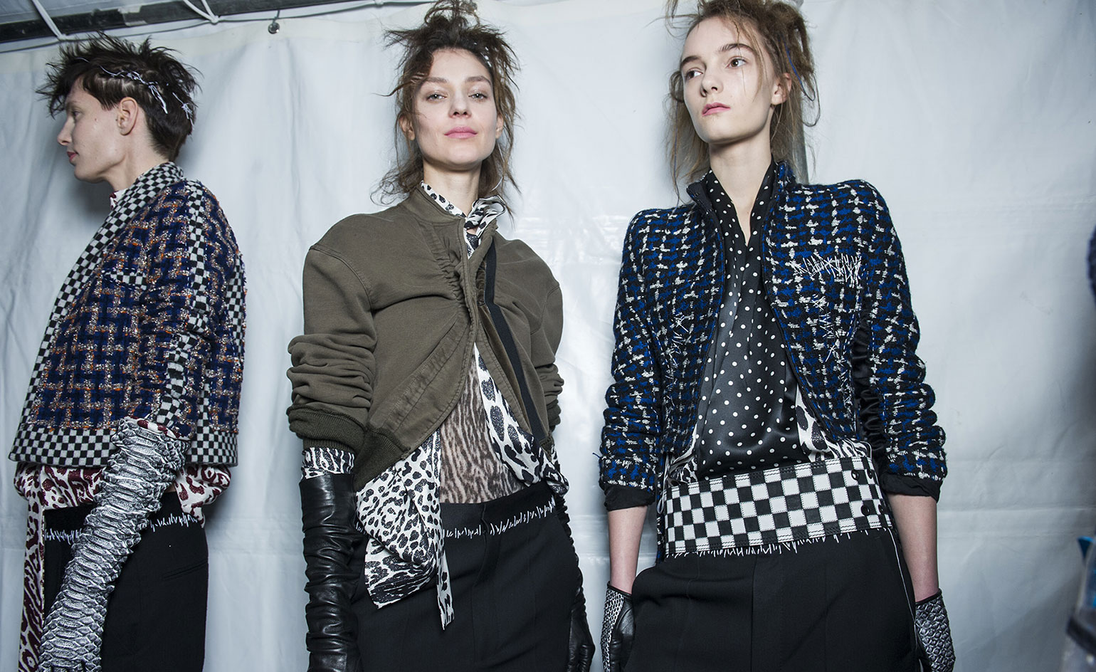 One woman wearing a black, blue and glittery jacket with checkerboard detailing, one in a brown jacket over animal print blouse, and one in a black, white and blue jacket over a black blouse with white polka dots and a checkerboard belt