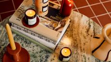 A marble coffee table with a stack of coffee table books, a pair of lit scented candles, a vase, and a taper