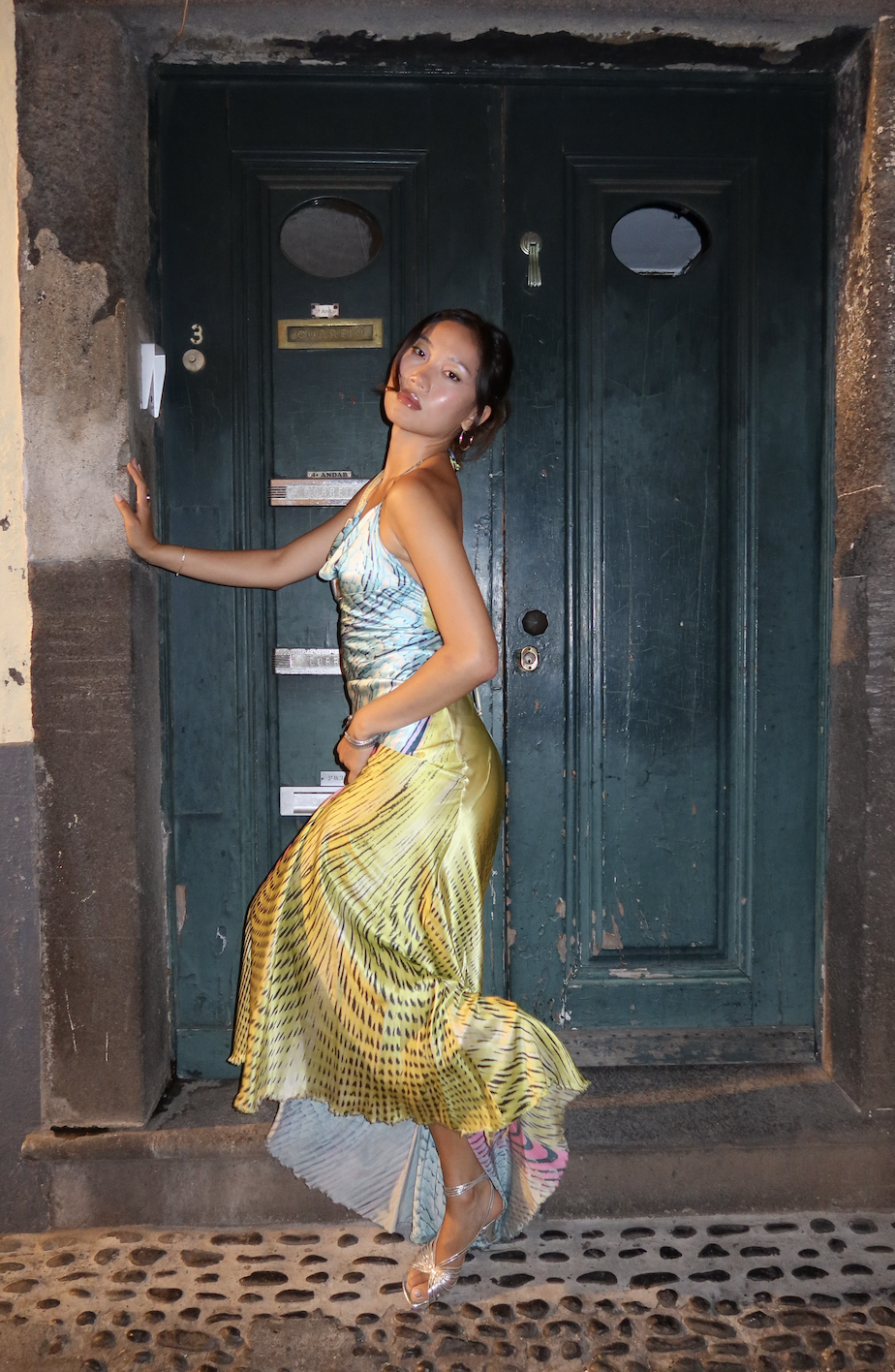 Vivian Li wearing a blue and yellow printed dress and silver heels on a cobblestone street