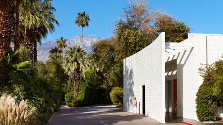 A man wearing a jacket stands in front of the entrance to The Parker Palm Springs on a sunny day