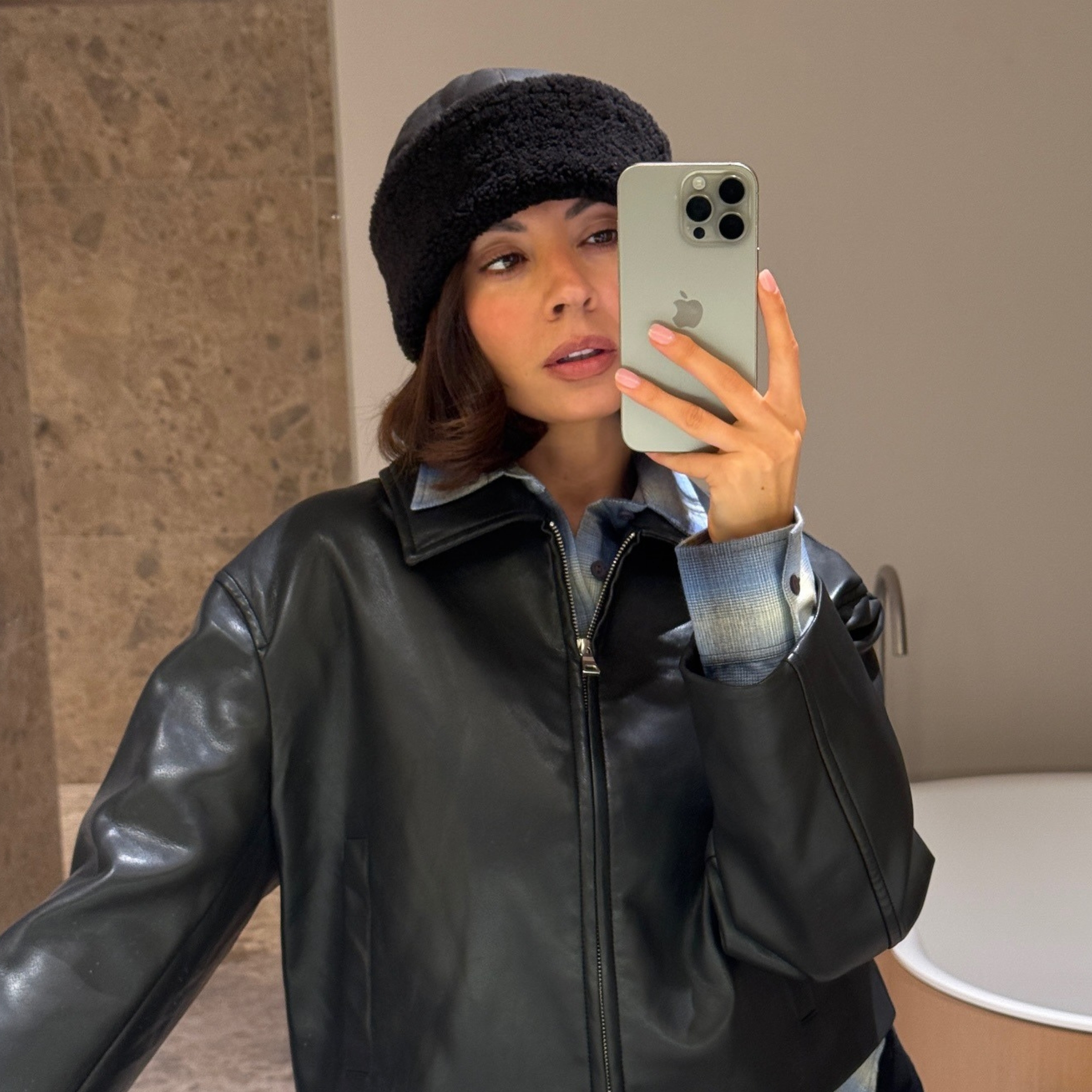 @smythsisters wearing a shearling hat, leather jacket and plaid shirt, in a selfie.