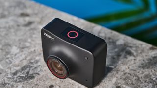 a black small 4K webcam with a red button photographed on a beige surface against a blue background