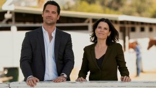 (L to R) Manuel Garcia-Rulfo as Mickey Haller, Neve Campbell as Maggie McPherson smiling and standing next to each other. 