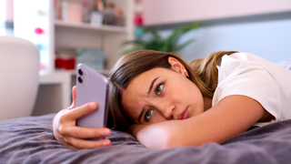 Depressed Teenage Girl Lying On Bed At Home Looking At Mobile Phone