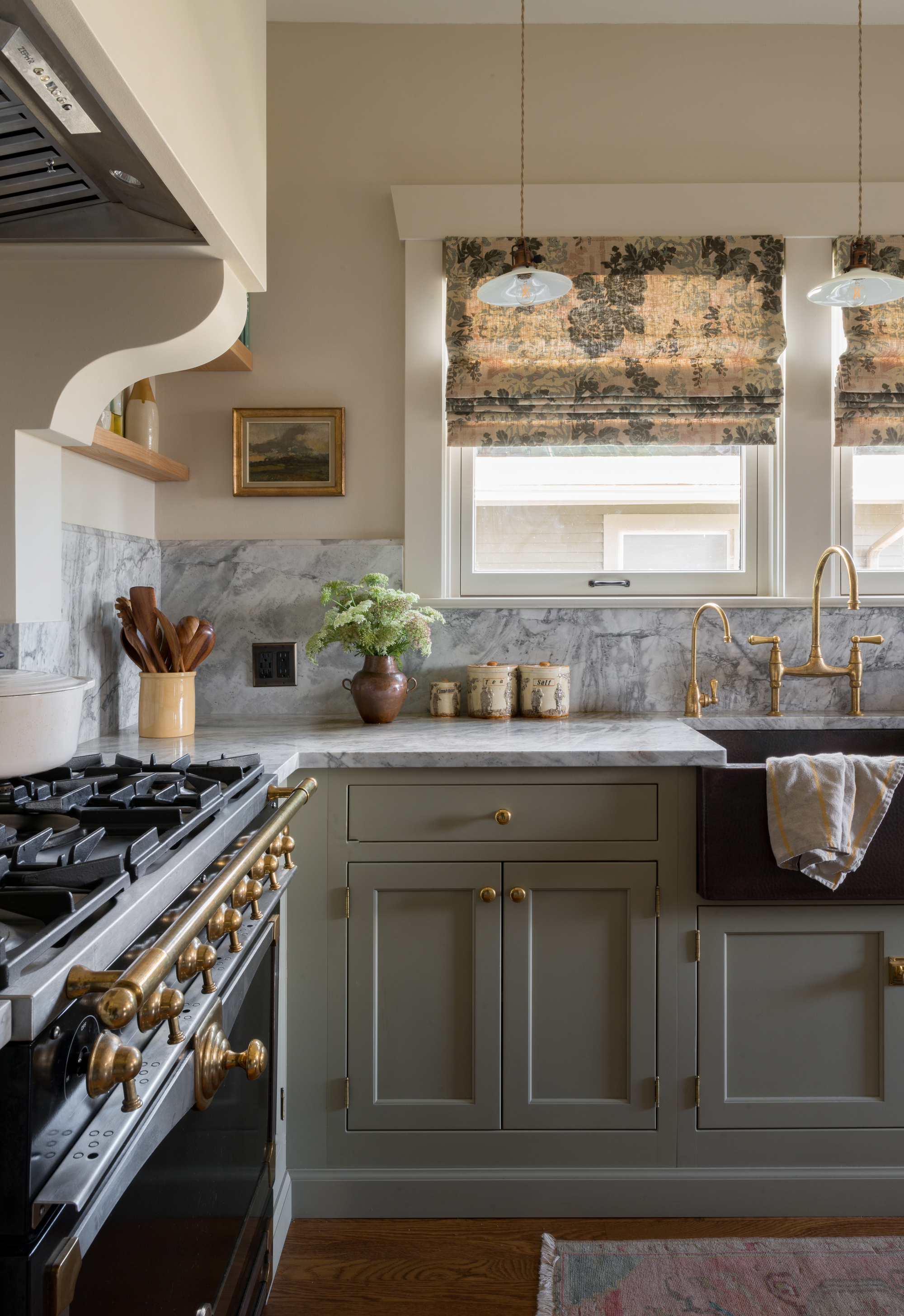 Image of the corner of a kitchen where the cabinetry is painted in a sage green and there are light gray marble countertops. 