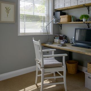 Grey walled home office with workstation, study lamp and stacks of grey storage boxes on wooden shelf