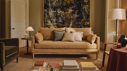 yellow living room with a butter yellow couch and a large tapestry hung behind styled with a green velvet armchair and little tables with lamps