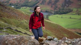 A woman wearing a bright Patagonia Women’s R1 CrossStrata Hoody walks up a rocky hillside.