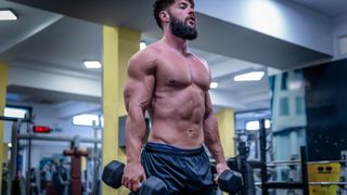 Shirtless bodybuilder in gym holding dumbbells