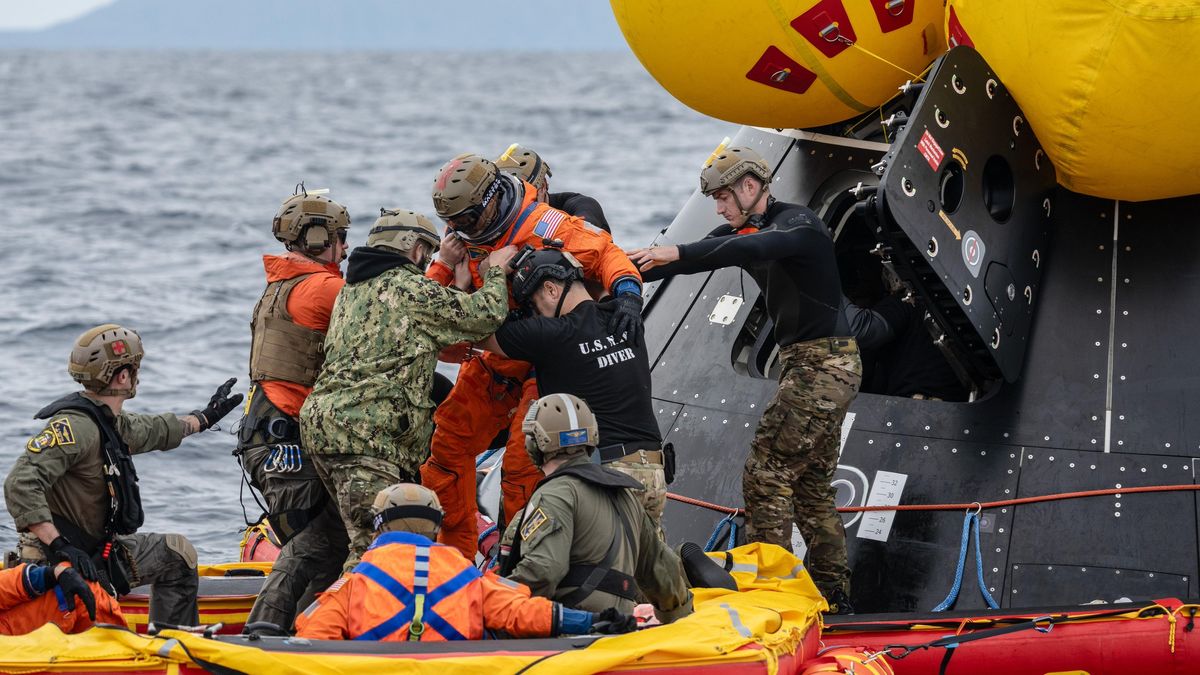 an astronaut is surrounded by people holding him in a life boat. behind him is an open spacecraft hatch. in far back is the ocean